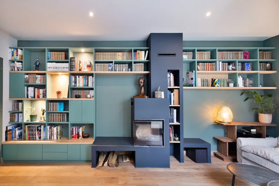 Bibliothèque sur mesure autour d’un insert avec façades vert amande et tablettes en bois clair